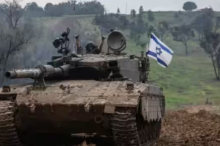 Seorang tentara Israel mengibarkan bendera dari sebuah tank saat kembali ke sisi perbatasan Israel /AFP