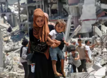 Seorang wanita Palestina menggendong putrinya saat dia berjalan melewati puing-puing rumah yang hancur selama serangan militer Israel, di tengah konflik Israel-Hamas, di Khan Younis di Jalur Gaza selatan 10 Juli 2024 /Reuters