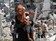 Seorang wanita Palestina menggendong putrinya saat dia berjalan melewati puing-puing rumah yang hancur selama serangan militer Israel, di tengah konflik Israel-Hamas, di Khan Younis di Jalur Gaza selatan 10 Juli 2024 /Reuters