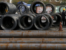 Seorang pekerja berdiri di dekat gulungan dan batang baja di fasilitas pengumpulan baja di Tokyo, Jepang /Reuters