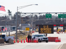 Petugas Bea Cukai AS berdiri di samping tanda yang menyatakan bahwa perbatasan AS ditutup di perbatasan AS/Kanada di Lansdowne, Ontario, pada 22 Maret 2020 /AFP